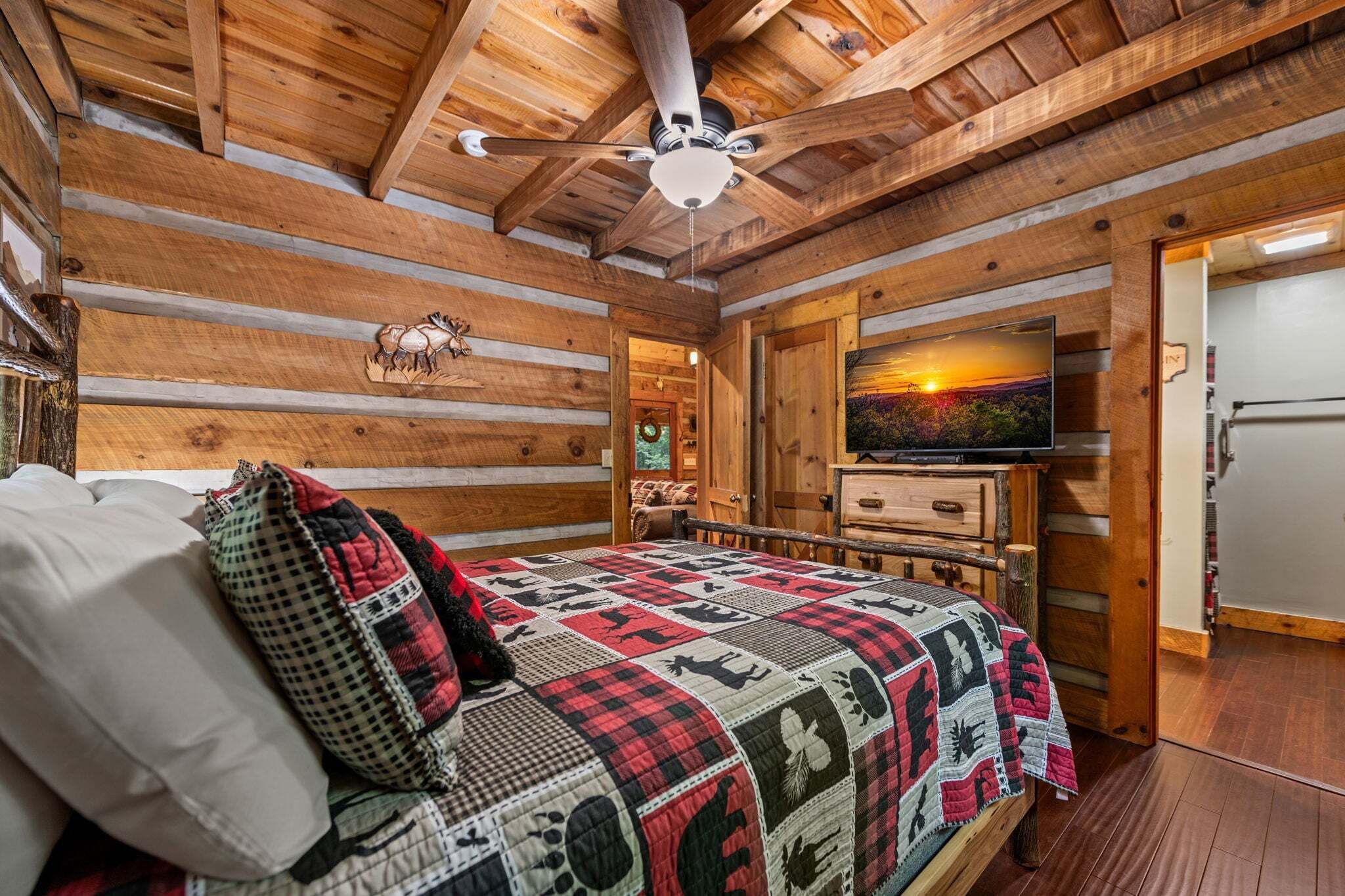 A log cabin interior with a bed, a ceiling fan, a television, and a fireplace.
