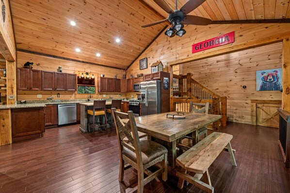 A cabin interior with a wooden interior, a kitchen area, a dining table with benches, and a sign that says 'GEORGIA'. - Bear Claw Lodge - Pet Friendly | Firepit | Outdoor Fireplace | Hot Tub (Cherry Log)