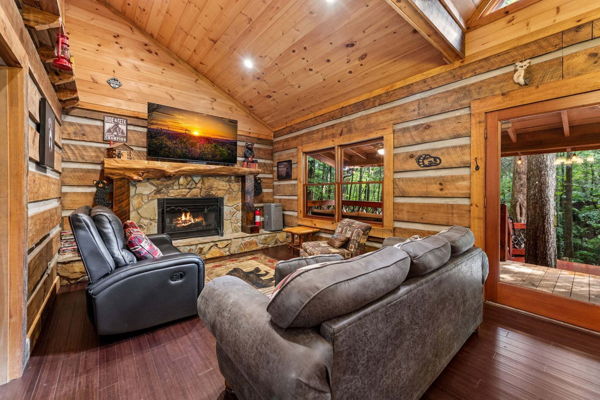 A log cabin interior with a stone fireplace, leather sofa, and a television mounted above it.