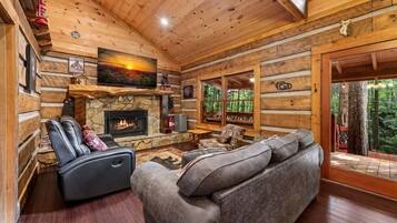 A log cabin interior with a stone fireplace, leather sofa, and a television mounted above it.