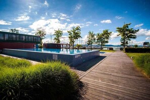 Ein Schwimmbad mit Holzterrasse, umgeben von Bäumen und einem Gebäude im Hintergrund.
