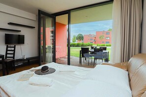 A hotel room with a bed, a TV, a desk, and a view of the outside.