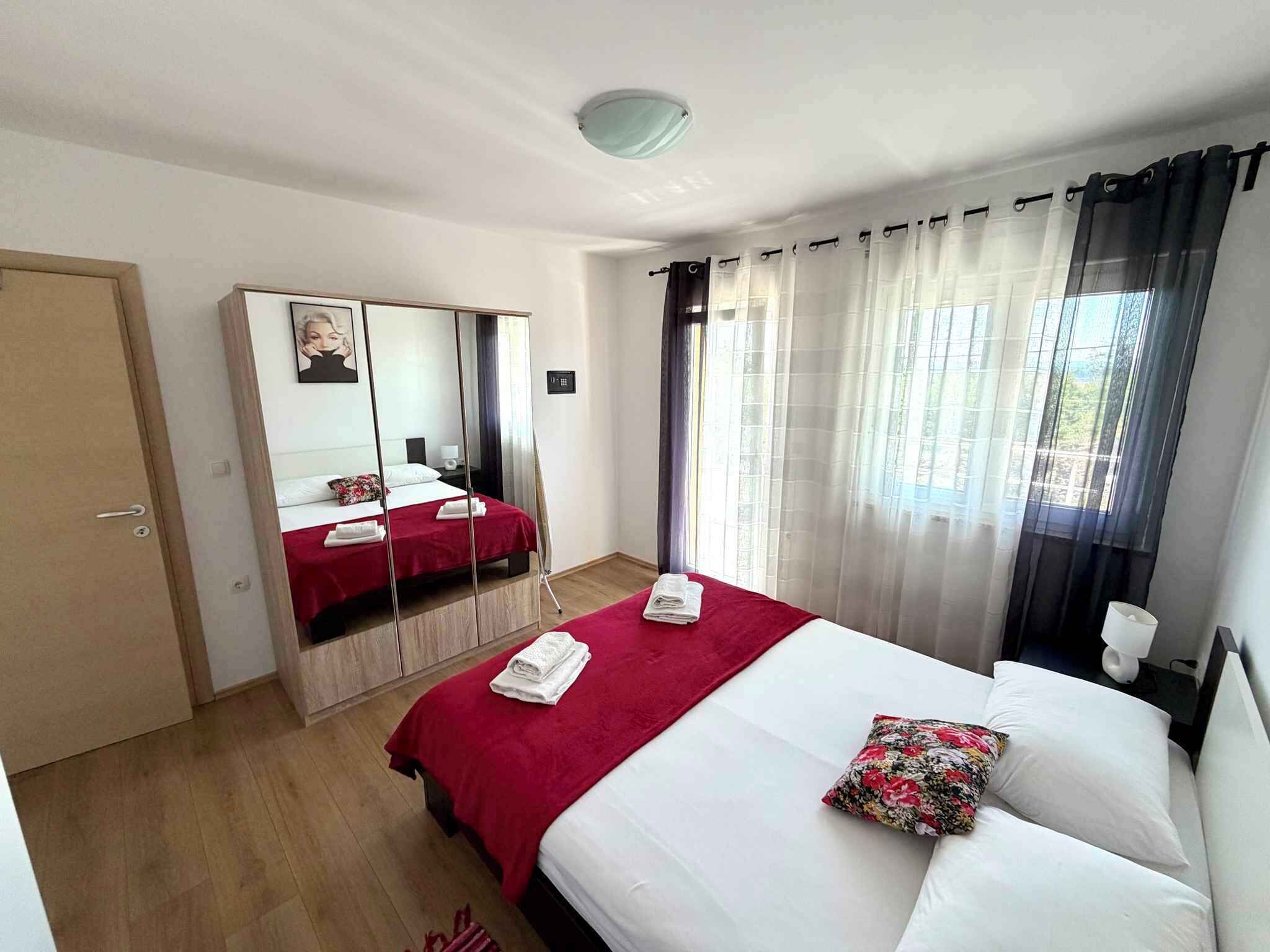 A hotel room with a bed, a wardrobe, a mirror, a bedside table, and a window with curtains.