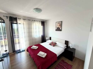 A hotel room with a bed, a bedside table, a nightstand, a window with curtains, and a ceiling light. - Modern holiday apartment with balcony (Jadranovo)