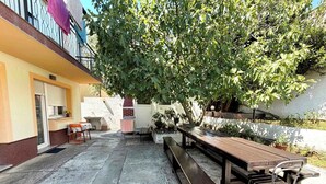 Eine Terrasse im Freien mit einem Holztisch und Bänken, umgeben von Blumentöpfen und einem Baum.