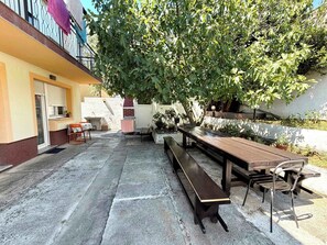 Eine Terrasse im Freien mit einem Holztisch und Bänken, umgeben von Blumentöpfen und einem Baum.
