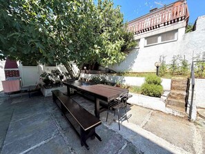 An outdoor patio with a wooden table and benches, surrounded by greenery and a white building with a balcony. - Modern holiday apartment with balcony (Jadranovo)