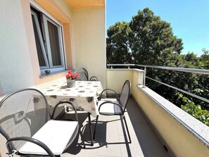 Un balcón con mesa y sillas, una ventana y vista a árboles.