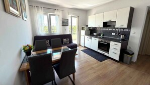 Eine moderne Küche mit weißen Schränken, ein Essbereich mit einem Glastisch und eine Sitzecke mit einem Sofa.