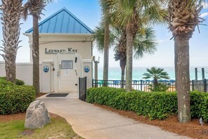 Une entrée fermée par un portail donnant accès à un immeuble portant l’inscription « Leeward Key », un chemin menant à l’entrée et une vue sur l’océan.