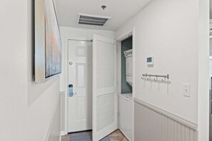 Ein Flur mit einer weißen Tür, einem Lüftungsgitter an der Decke, einem Kleiderständer und einem kleinen Fenster mit Blick.
