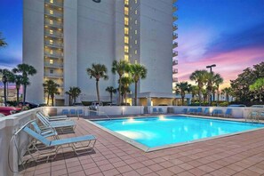 A swimming pool with lounge chairs, palm trees, and a tall building in the background. - 805 Gulf Front Views & Rare Gulf Front Pool ~ Gorgeous 2-bdm ~ Book Oct 23rd (Destin)