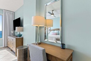 Ein Hotelzimmer mit einem Holztisch, einem Spiegel, einer Lampe, einem Fernseher und Blick auf den Ozean.
