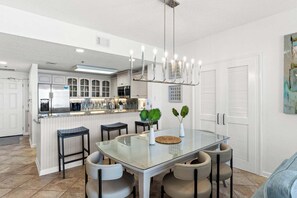 A modern kitchen with a glass dining table, bar stools, and pendant lighting. - 805 Gulf Front Views & Rare Gulf Front Pool ~ Gorgeous 2-bdm ~ Book Oct 23rd (Destin)