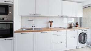 Eine moderne Küche mit weißen Schränken, einer Holzarbeitsplatte, einem eingebauten Backofen, einer Waschmaschine und einem Spülbecken.