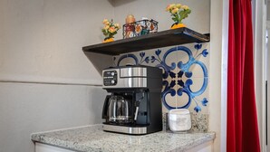 Une cuisine équipée d’une machine à café, d’un meuble blanc, d’un crédence décorative en carreaux et d’un rideau rouge.