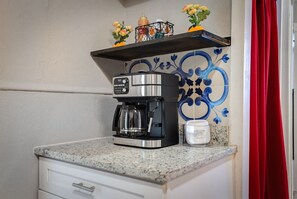 Eine Küche mit Kaffeemaschine, einem weißen Schrank, einer dekorativen Fliesenrückwand und einem roten Vorhang.