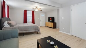 Une chambre à coucher avec un lit, une télévision, un ventilateur de plafond et une fenêtre avec des rideaux.