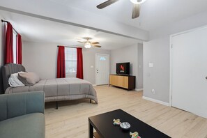 Ein Schlafzimmer mit einem Bett, einem Fernseher, einem Deckenventilator und einem Fenster mit Vorhängen.