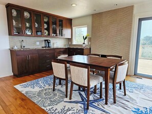 A modern kitchen with dark wooden cabinets, a granite countertop, and a dining area with a wooden table and four chairs. - Pool Sea and Sunshine (Aptos)
