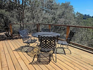 A wooden deck with a round table and four chairs, surrounded by a metal railing. - Pool Sea and Sunshine (Aptos)