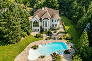 A large house with a swimming pool, surrounded by lush greenery.