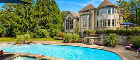 Une grande piscine avec un jacuzzi, entourée d’un jardin aménagé où poussent différentes plantes et fleurs.