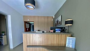 A reception desk with a wooden finish, a framed picture on the wall, and a black lamp beside it. - Hotel Azur (Fos-sur-Mer)