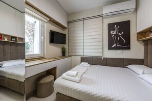 Ein Schlafzimmer mit einem Bett, einem Schreibtisch, einem Fernseher und einem Fenster.