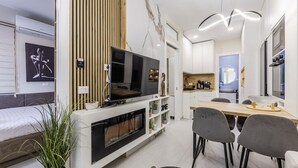 Een moderne woonkamer met een flatscreen televisie, een eethoek met een houten tafel en stoelen, en een keuken op de achtergrond.