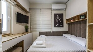 Een moderne slaapkamer met een bed, bureau, televisie en raam.
