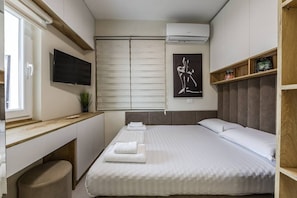 Ein modernes Schlafzimmer mit Bett, Schreibtisch, Fernseher und Fenster.