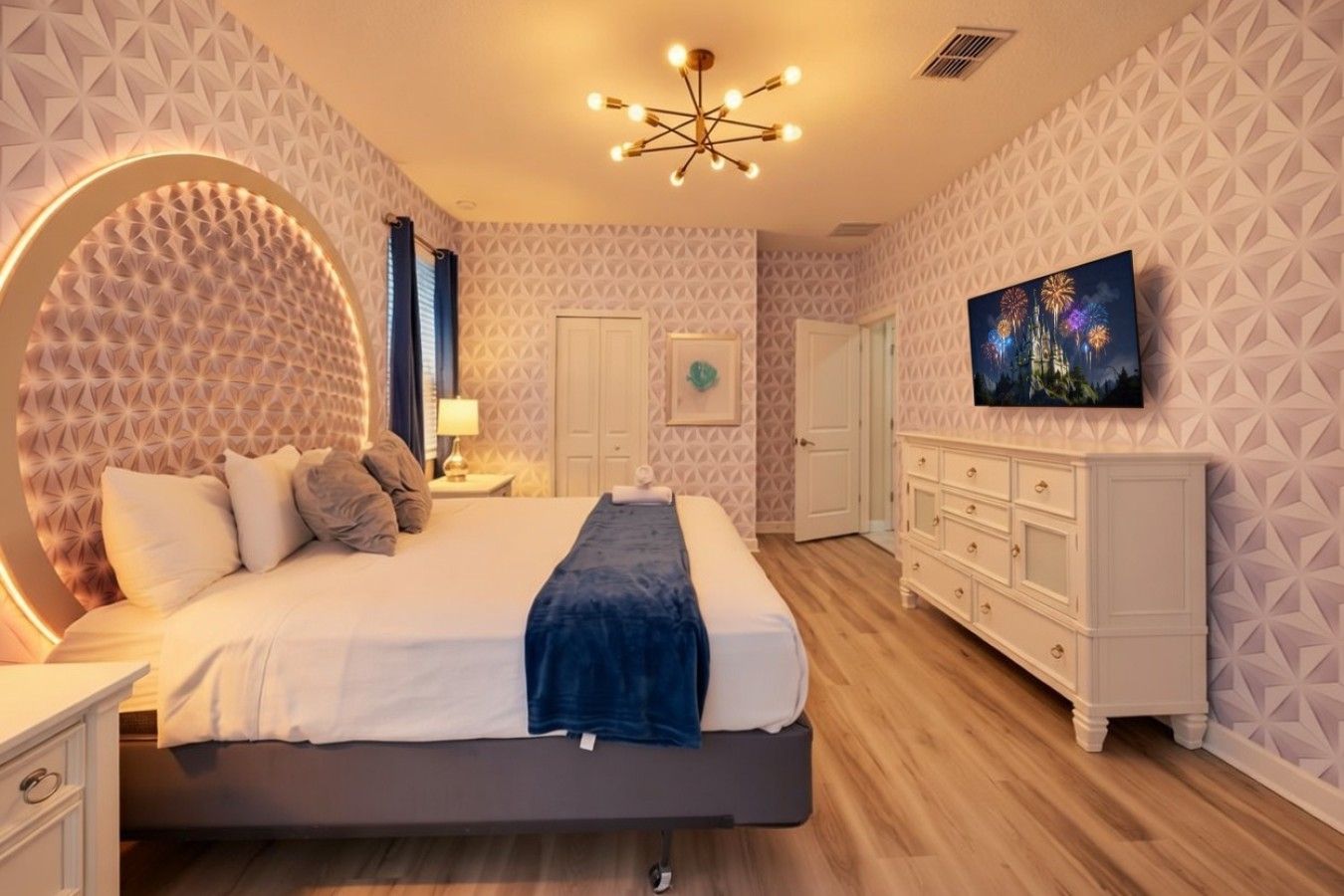 Quarto moderno com uma cama grande, cômoda, televisão e paredes com padrão geométrico.