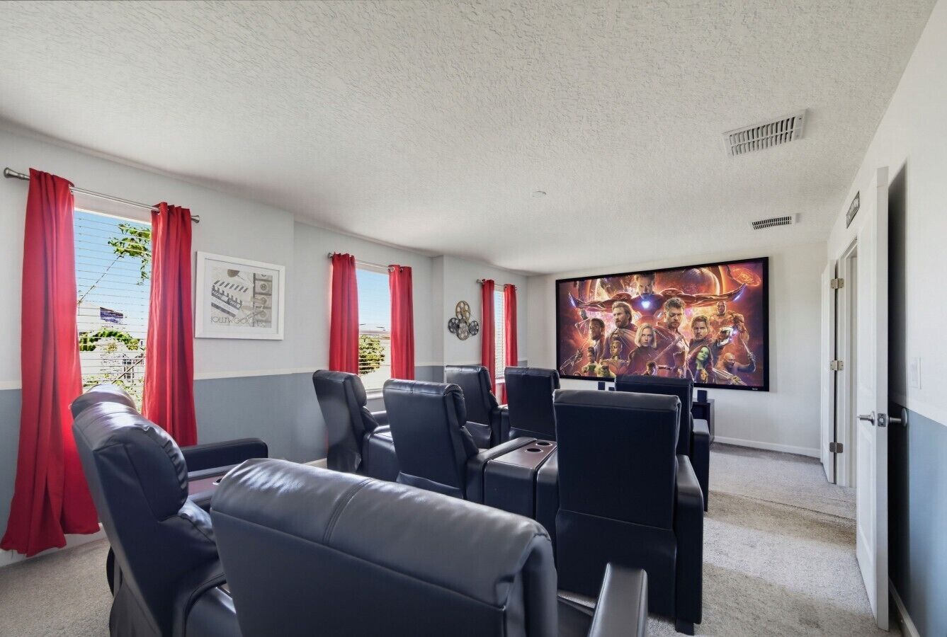 A room with a large flat-screen TV, black leather seating, red curtains, and a framed picture on the wall.