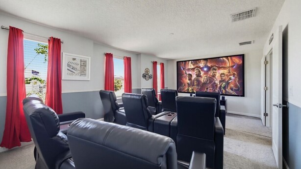 Ein Zimmer mit großem Flachbildfernseher, schwarzen Ledersesseln, roten Vorhängen und einem gerahmten Bild an der Wand.
