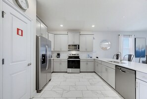 A modern kitchen with white cabinets, stainless steel appliances, and a tiled floor. - Champions Legacy 8BR Pool Villa (Kissimmee)