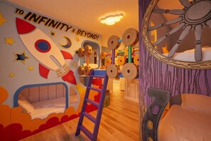 Une salle de jeux pour enfants avec une fresque murale représentant une fusée, une structure de jeu en bois et un lit avec une échelle.