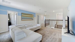 Ein modernes Wohnzimmer mit einem weißen Modulsessel, einem Flachbildfernseher und einem farbenfrohen abstrakten Gemälde an der Wand.