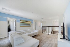 A modern living room with a white sectional sofa, a flat-screen TV, and a colorful abstract painting on the wall. - Champions Legacy 8BR Pool Villa (Kissimmee)