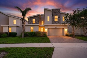 A modern two-story house with a garage, well-maintained lawn, and a sunset sky. - 9 Bedroom Themed Villa Sleeps 24 with Private Pool Spa and Arcade (Kissimmee)