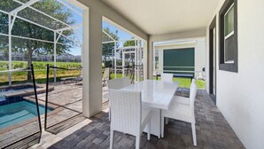 Ein Außenbereich mit Terrasse, Pool, weißen Korbmöbeln und einem überdachten Sitzbereich.