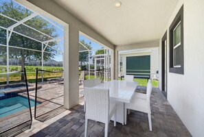 An outdoor patio area with a pool, white wicker furniture, and a covered seating area. - Champions Legacy 8BR Pool Villa (Kissimmee)