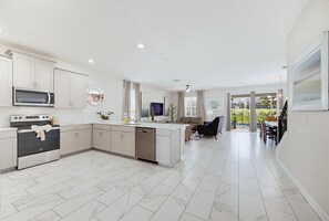 A modern kitchen with a central island, built-in appliances, and a dining area with a view. - 9 Bedroom Themed Villa Sleeps 24 with Private Pool Spa and Arcade (Kissimmee)