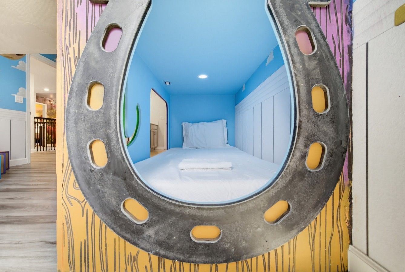 A room with a bed centered in a circular window-like structure, a door to the left, and a hallway leading to another room.