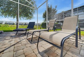 Mobilier d’extérieur avec des structures métalliques et des coussins en tissu, installé sur une terrasse en pierre avec une structure en verre en arrière-plan.