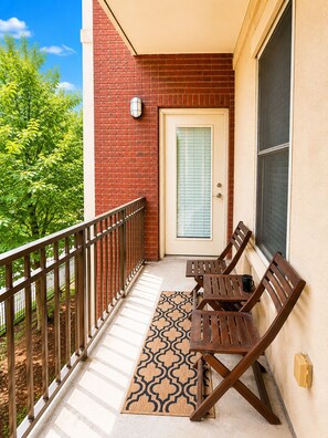 Ein Balkon mit Holztisch und -stühlen, eine Tür mit Fenster und eine Backsteinmauer.