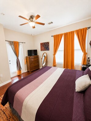 Een slaapkamer met een bed, een plafondventilator, een dressoir, een televisie en een raam met gordijnen.