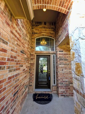 Un ingresso in mattoni con una porta vetrata, un piccolo balcone e un tappetino di benvenuto.