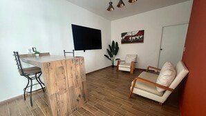 A living room with a wooden floor, a TV mounted on the wall, a chair, a sofa, and a plant. - 🏙️ EXECUTIVE APARTMENT FOR RENT | 2 BEDROOMS | CENTRAL LOCATION (Chihuahua)