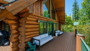 Une cabane en rondins avec une terrasse, un espace salon extérieur et une vue sur les arbres.